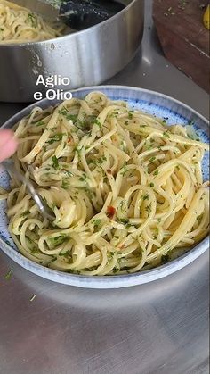 a bowl of pasta with parsley on top in front of two pans of food