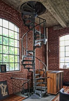 a spiral staircase in the middle of a room with brick walls and wooden flooring