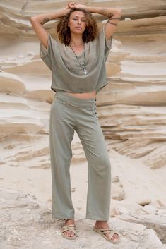 a woman standing on top of a sandy beach next to the ocean with her hands behind her head