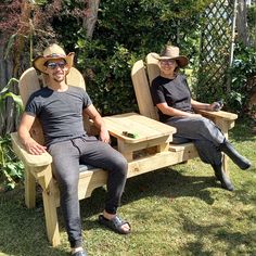 two people sitting on wooden chairs in the grass with one person wearing a hat and sunglasses