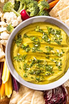 a bowl filled with yellow dip surrounded by vegetables and crackers