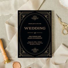 a black and gold wedding card on top of a table next to some paper scissors