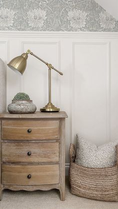 a nightstand with a lamp on it next to a basket and pillow in the corner