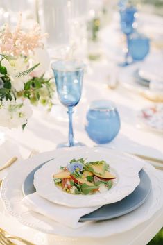 the table is set with blue and white plates, silverware, and flowers in vases