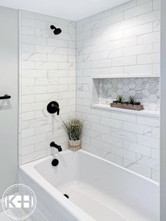 a white bathroom with black fixtures and marble tiles on the walls, along with a plant