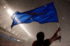 a man holding up a blue flag in the rain at a soccer game on a snowy day