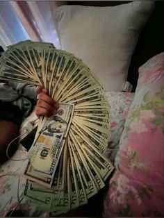 a person laying on a bed holding a fan of money