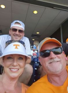 three people are sitting in the stands at a baseball game, one is wearing a tennessee hat