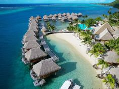 an aerial view of a beach resort with thatched roofs and palm trees in the water