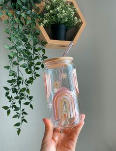 a person holding up a mason jar with a straw in it and a plant hanging from the top