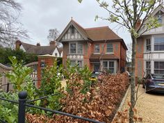 a black car parked in front of a house next to a fence and trees with leaves on it