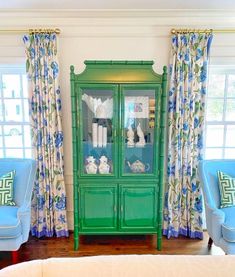 a green china cabinet sitting in the corner of a living room next to two blue chairs