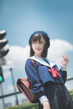 a young woman dressed in a sailor outfit and holding a brown bag standing next to a traffic light