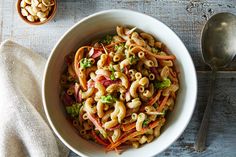 a bowl filled with pasta and vegetables next to two spoons on top of a wooden table