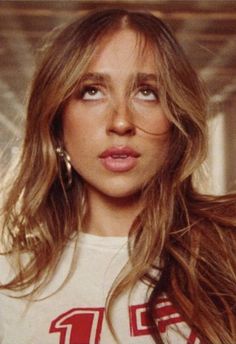 a close up of a person with long hair wearing a white t - shirt and earrings