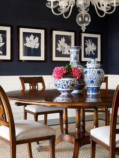 a dining room table with two vases on top of it next to chairs and chandelier