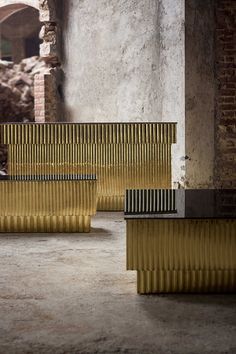 two gold benches sitting in an old building with brick walls and arches on the sides