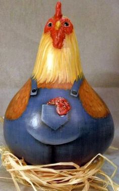 a ceramic chicken sitting on top of a blue egg with straw around it's legs