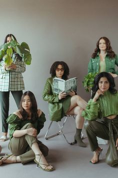 four women are sitting in chairs and one is holding a book while the other woman holds a plant