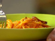 a green bowl filled with pasta next to a fork and a person's hand