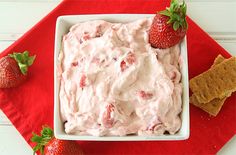 a white bowl filled with strawberry fluff next to two strawberries and crackers