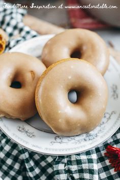 three glazed donuts on a white plate with green and red checkered table cloth