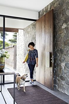 a woman is walking her dog on the front porch with large doors and stone walls