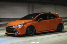 an orange car driving down a street at night