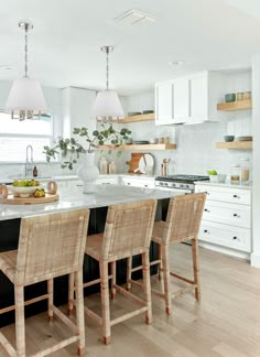 a kitchen with white cabinets and wooden chairs next to a center island in the middle