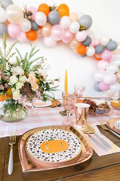 a table set with plates, silverware and balloons