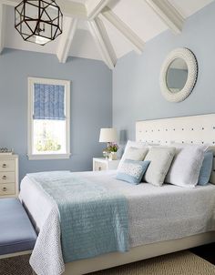 a bedroom with blue walls, white bedding and a mirror above the headboard