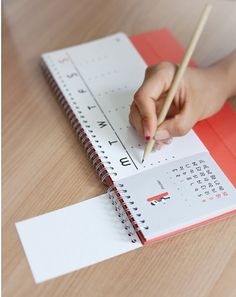 a child's hand holding a pencil and writing on a calendar with red paper