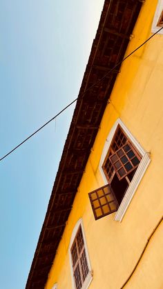 an old yellow building with two windows and power lines in the foreground, against a blue sky