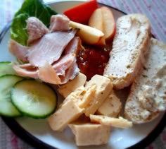 a white plate topped with meat, cheese and cucumber on top of a table