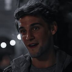 a close up of a person in a dark room with lights on the wall behind him