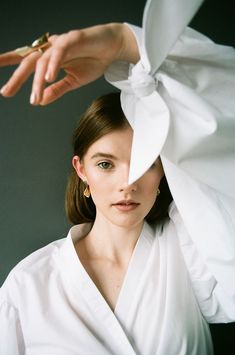 a woman is wearing a white shirt with a bow on it's head and holding her hand over the top of her head