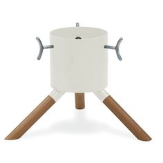 a white pot with two wooden legs and handles on it's side, sitting on top of a tripod