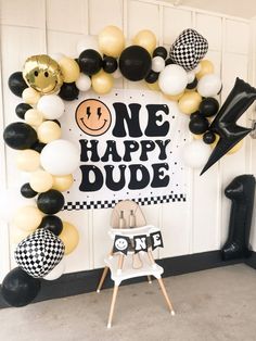 a black and white balloon arch with one happy dude sign in the center surrounded by balloons