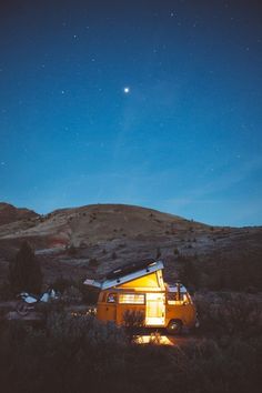 a yellow camper van parked in the middle of a field under a night sky