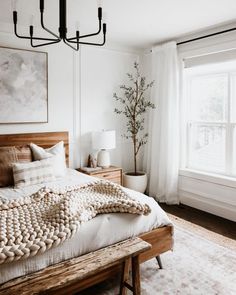 a bedroom with white walls and wooden bed frame, chandelier, window, and rug on the floor