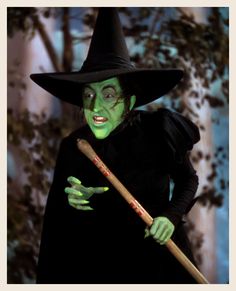 a woman dressed in green and black holding a wooden stick while wearing a witch costume