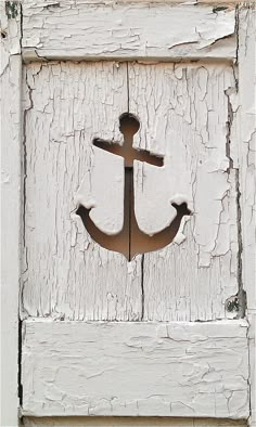 an anchor painted on the side of a white wooden door with paint peeling off it