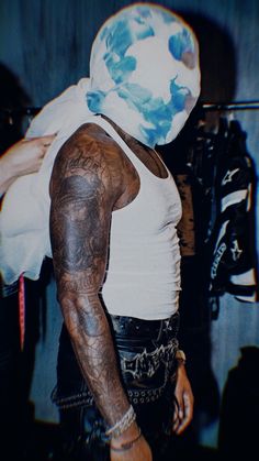 a man with tattoos and a white mask on his face is standing in front of a camera