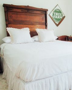 there is a bed with white sheets and pillows on top of it, next to a tree farm sign