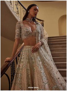 a woman in a gold and silver lehenga standing next to some stairs with her hands on her hips