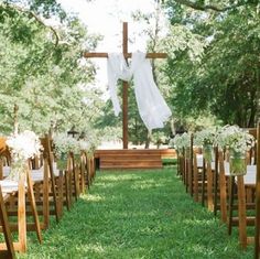 an outdoor ceremony setup with white flowers and greenery on the grass, in front of a wooden cross