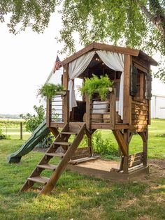 a wooden play set with a tent and slide in the grass next to a tree