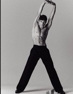 a shirtless man in black pants stretching his arms