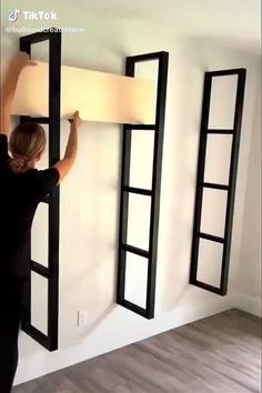 a woman is holding up some black frames on the wall, and she's working on it