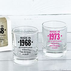 two personalized glass tumblers are shown next to a box of birthday candles on a white wooden table